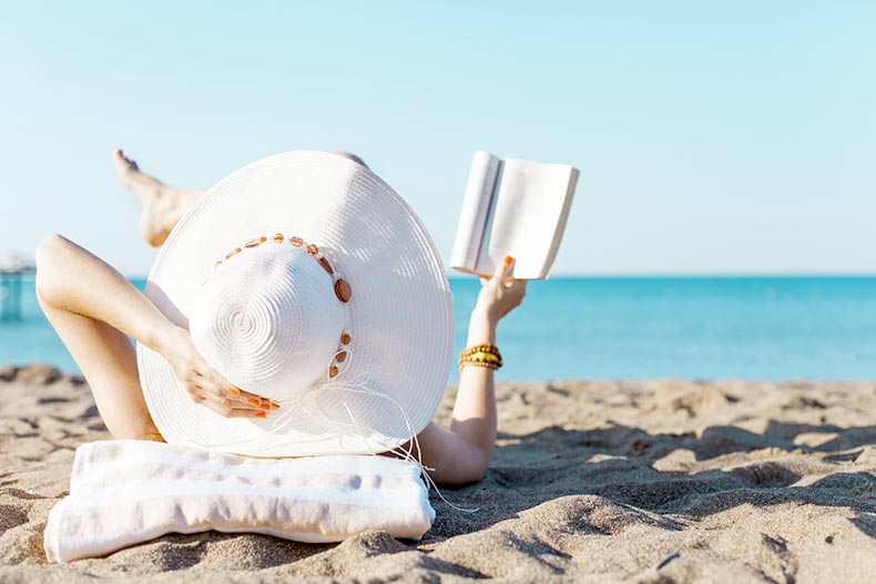 Woman in a hat reading a book on a beach