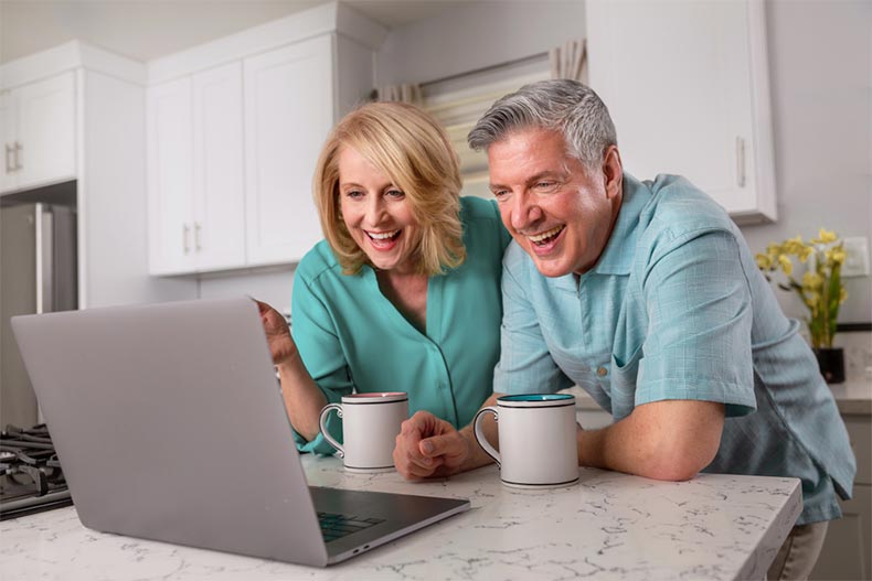 Active adult couple smiling while video chatting in the kitchen