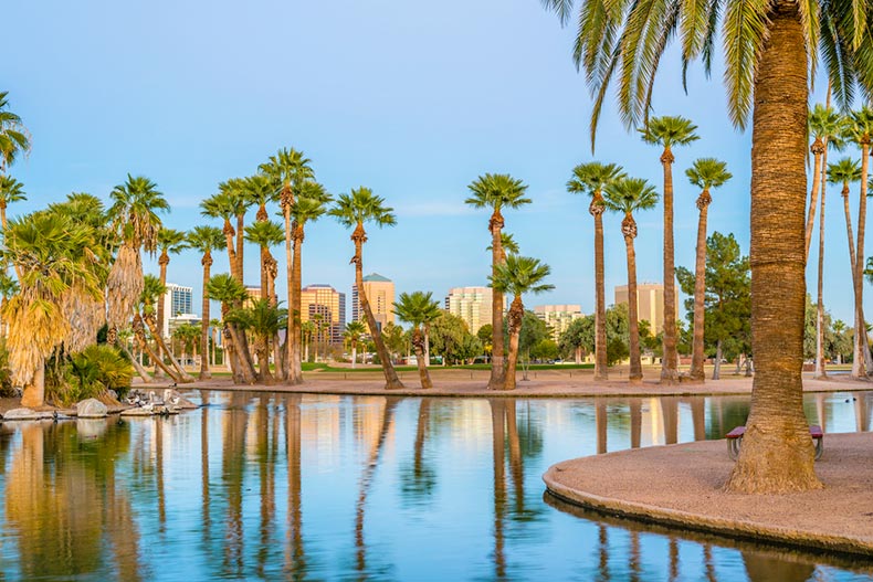 View of buildings in Phoenix, Arizona from across a lagoon surrounded by palm trees in Encanto Park