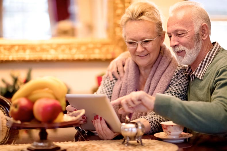 An active adult couple using a tablet to shop online for a home in a 55+ community