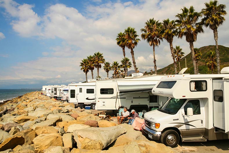Two active adults sitting beside a line of RVs on the rocky beaches of Faria Beach National Park in Venture, California