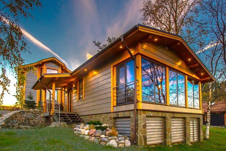 A wooden cottage with panoramic windows on the property of a larger home