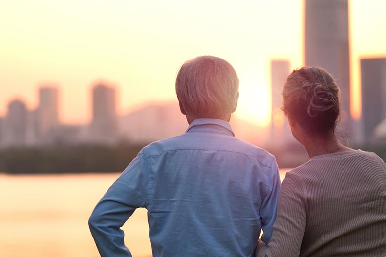 Rear view of a senior couple by a river looking at the sunset over a city skyline