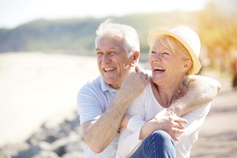 A senior couple with their arms around each other smiling and laughing while on a beach