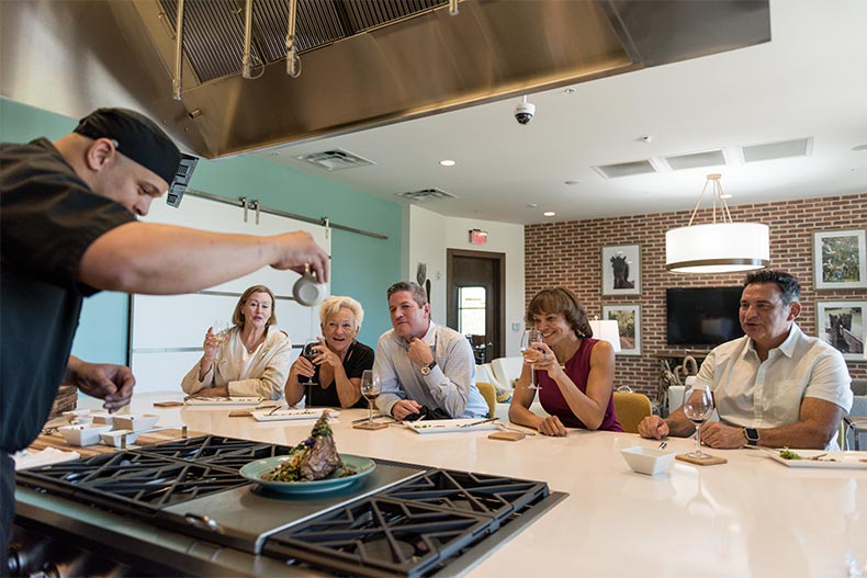 A group of residents enjoying a cooking demonstration in the community kitchen at Trilogy at Ocala Preserve in Ocala, Florida