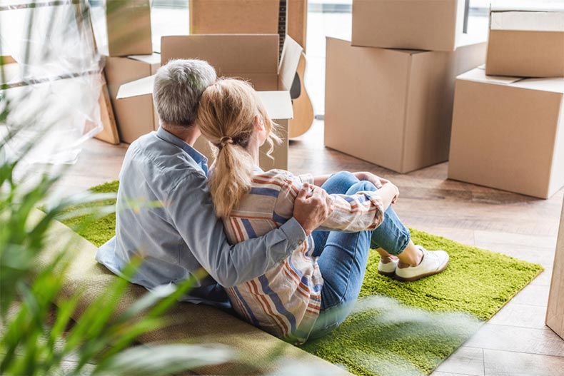 An active adult couple embracing while sitting on carpet and downsizing into a new house