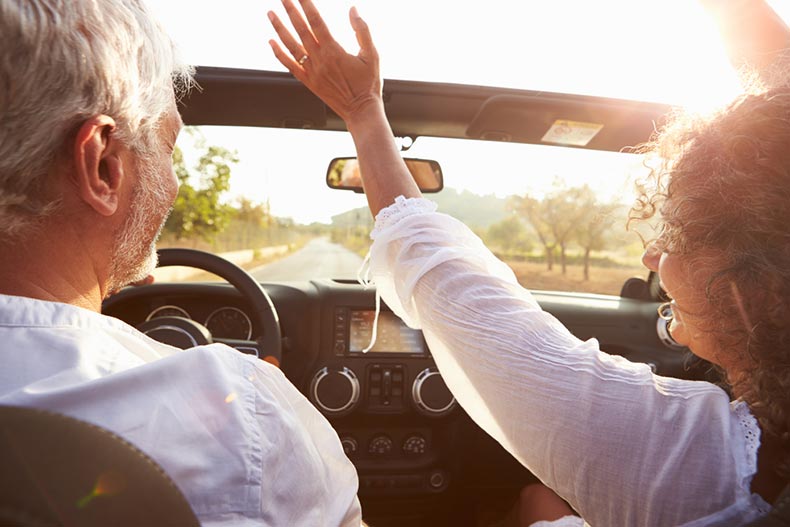 An active adult couple driving in a convertible and enjoying their early retirement