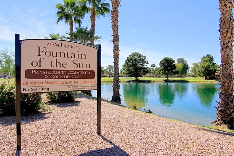 A blue sky over a pond surrounded by trees beside the sign for Fountain of the Sun in Mesa, Arizona