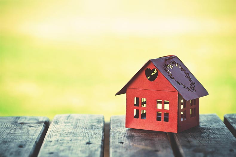 A small, red model of a house on a wood table with a sunny background