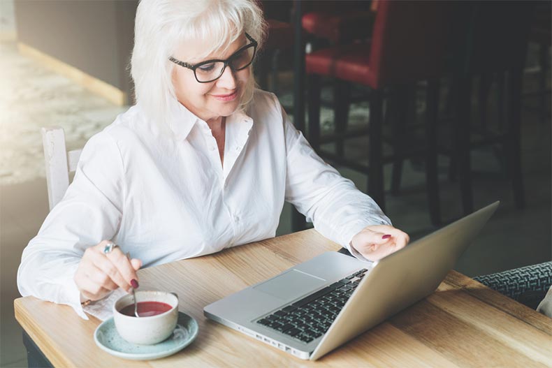 A smiling businesswoman submitting her retirement notice on a laptop while drinking tea