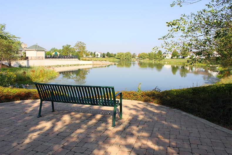 View of a bench facing a pond surrounded by landscaped greenery at Grand Haven in Romeoville, Illinois