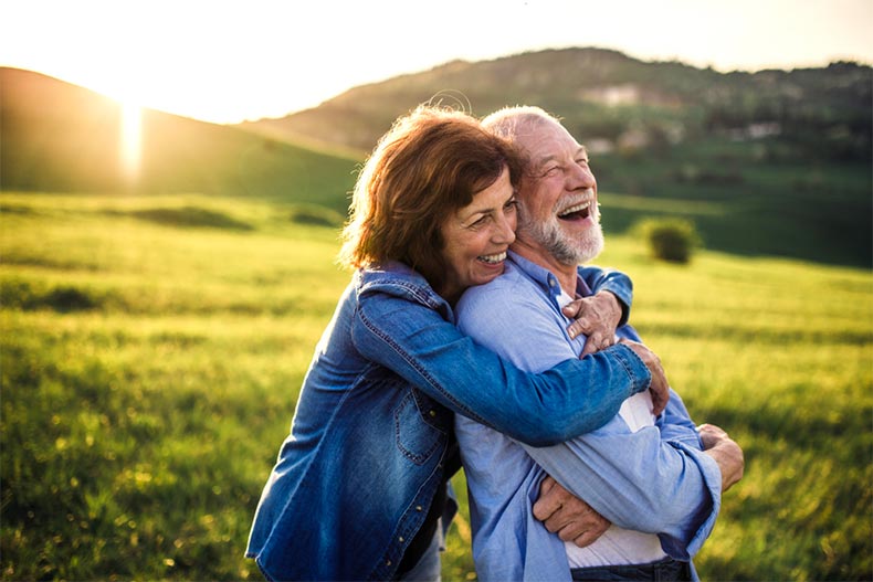 An older couple hugging and laughing in an open field