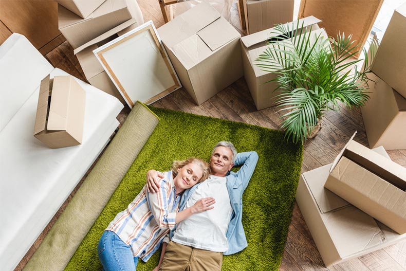 High angle view of a happy senior couple lying on a green carpet surrounded by moving boxes