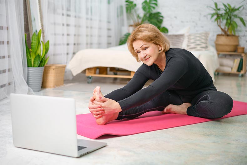 An active adult woman doing yoga at home with her laptop