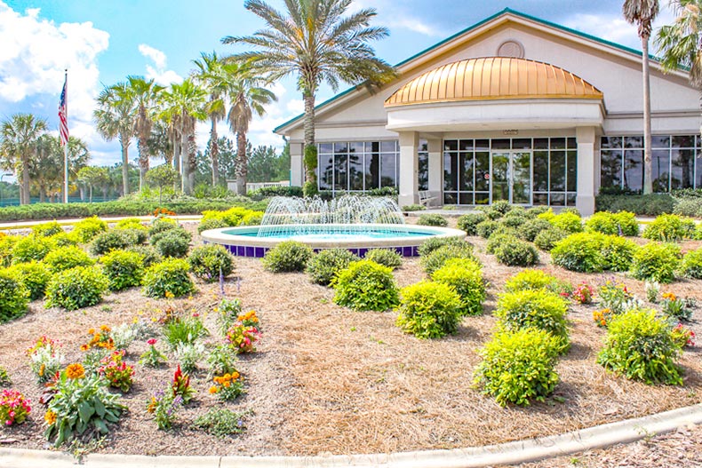 Exterior view of groomed landscaping, a flagpole, and palm trees outside the clubhouse at On Top of the World in Ocala, Florida