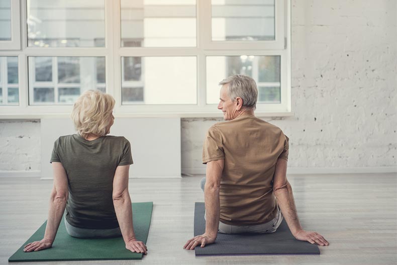 Older man and woman sitting on yoga mats with their back to camera