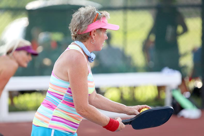An active adult pickleball player prepares to serves as she competes in a tournament
