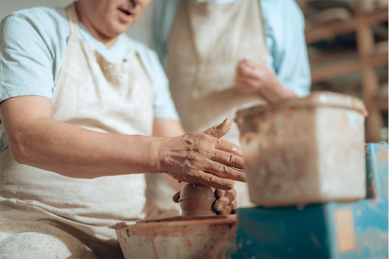 A senior man throwing a pot on a pottery wheel at a 55+ community ceramics studio