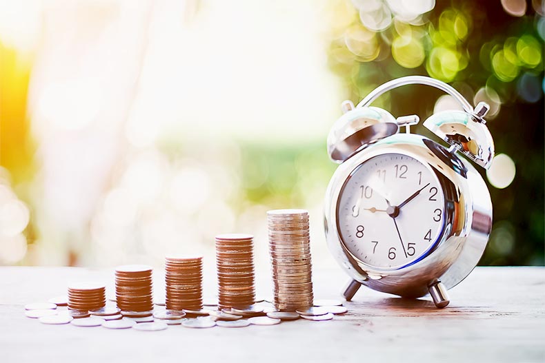 Close up of five progressively larger stacks of coins beside an alarm clock