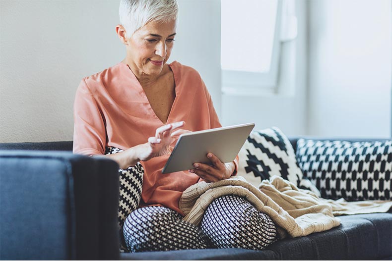 Older woman sitting comfortably on couch looking at tablet