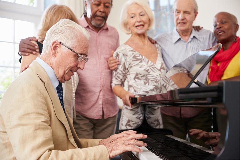 A group of seniors standing around a piano and singing along