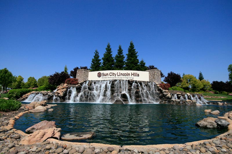 View of the community sign at Sun City Lincoln Hills with a water feature and landscaping surrounding it.