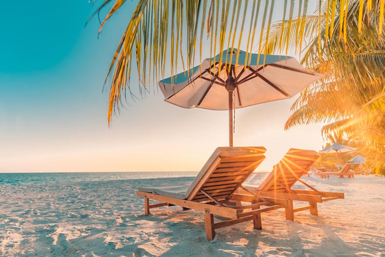 Two lounge chairs under a beach umbrella on a tropical beach