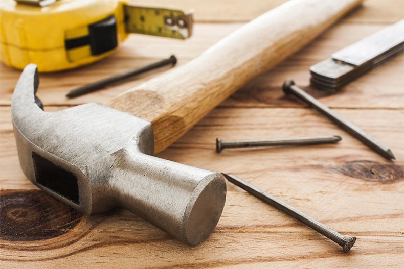 Closeup on a hammer, a tape measure, a ruler, and nails on a wooden table