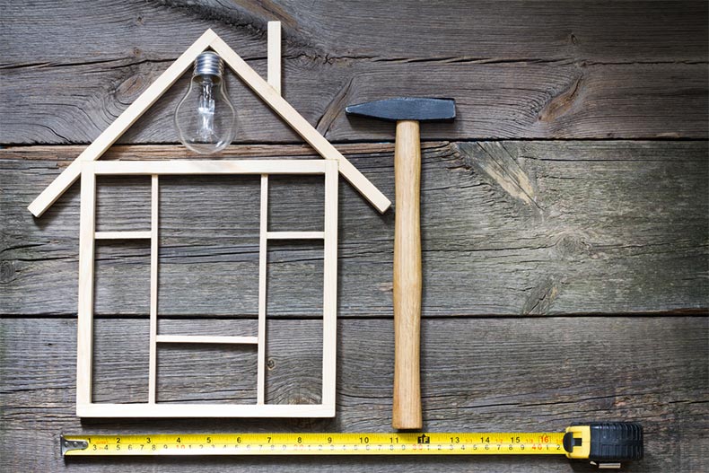 A tape measure and a hammer beside the wooden outline of a house