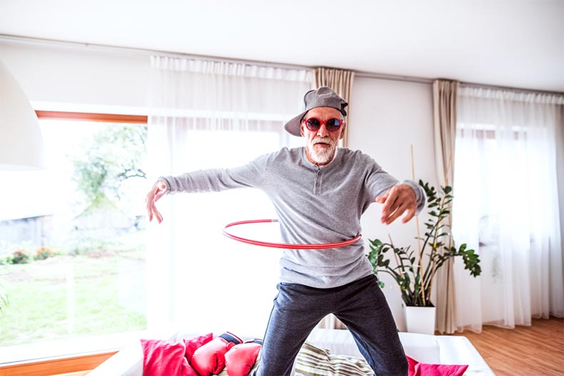 A senior man in silly sunglasses having fun with a hula hoop at home