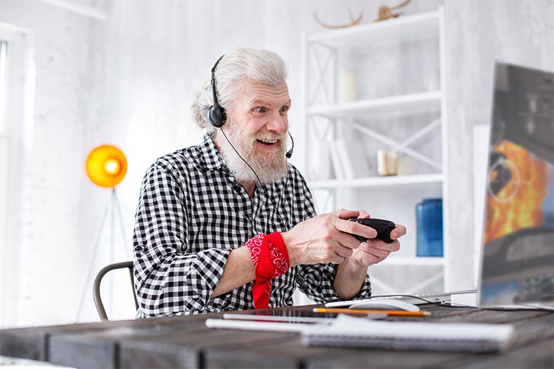 An older man with a headset on excitedly playing video games at his desk
