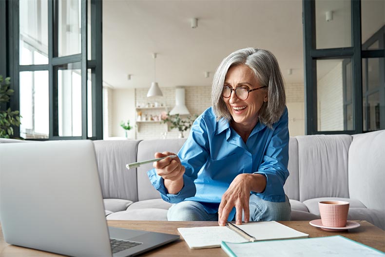 A smiling older woman video calling on a laptop while working from home
