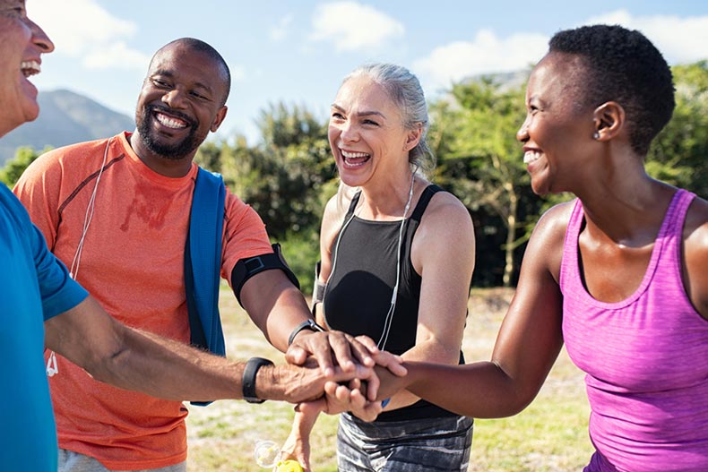 Active adults putting their hands together at the end of a fitness class in their 55+ community