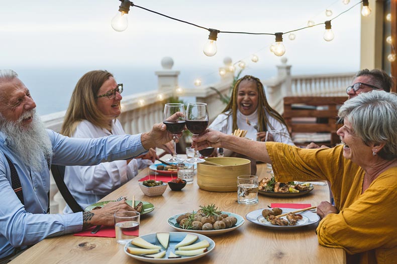 Senior friends dining together and toasting with wine on a patio in a 55+ community