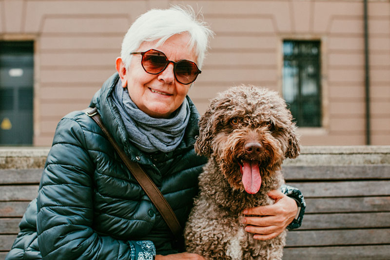 Older woman and her dog happily sitting on a park bench