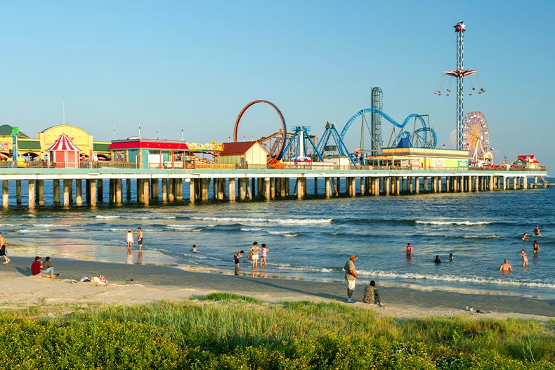 Distant view of beachgoers in Galveston, Texas next to a pier with amusement park rides