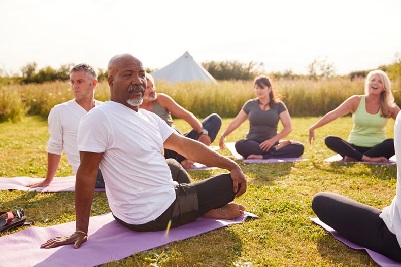 Female teacher leading a group of mature men and women in an outdoor yoga class