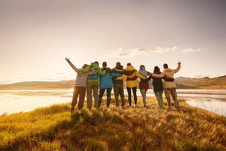 A group of active adult friends standing and hugging in the mountains near a lake