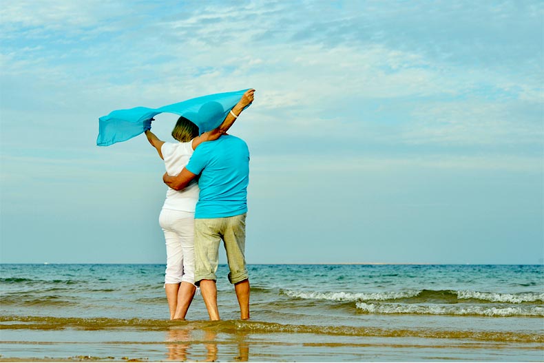 Active adult couple standing on a beach while looking out over the waves
