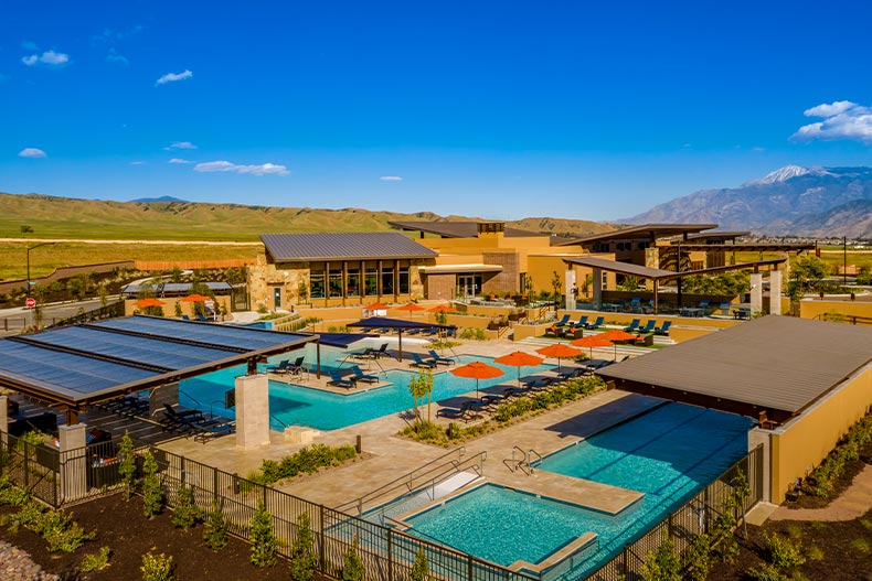 Overhead view of the recreation center in Altis with multiple resort-style pools, patios, awnings with solar panels, a clubhouse, and views of the nearby mountain range, located in Baeumont, California
