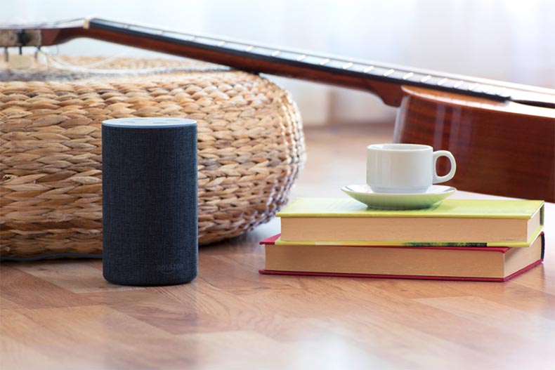 An Amazon Echo in a living room beside books, a teacup, and a guitar.