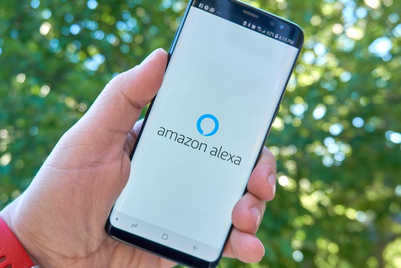 A hand holding a Samsung Galaxy S8 and opening the Amazon Alexa android app