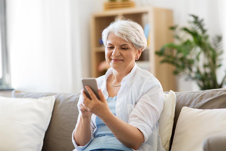 A senior woman sitting on a couch and downloading a retirement app on her smartphone