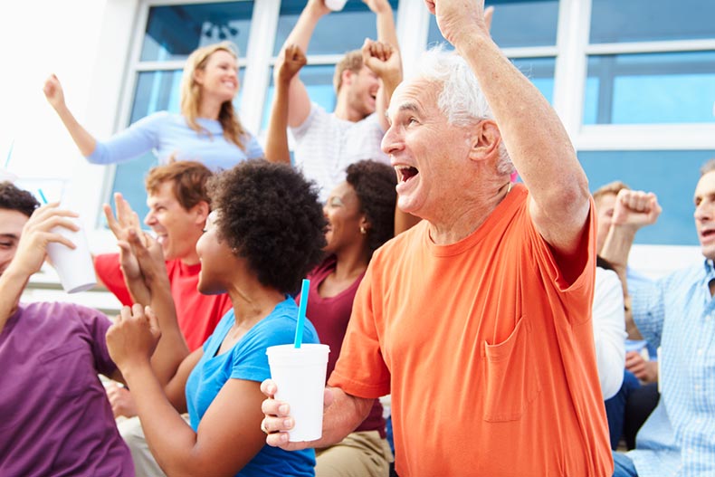 A senior man in a crowd of spectators cheering at an outdoor sports event