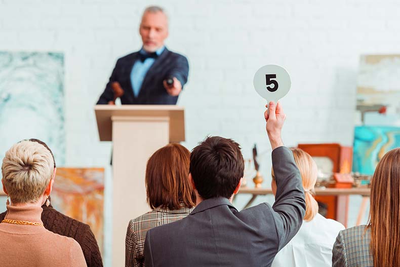 Back view of a bidder raising a number five paddle to an auctioneer at an auction