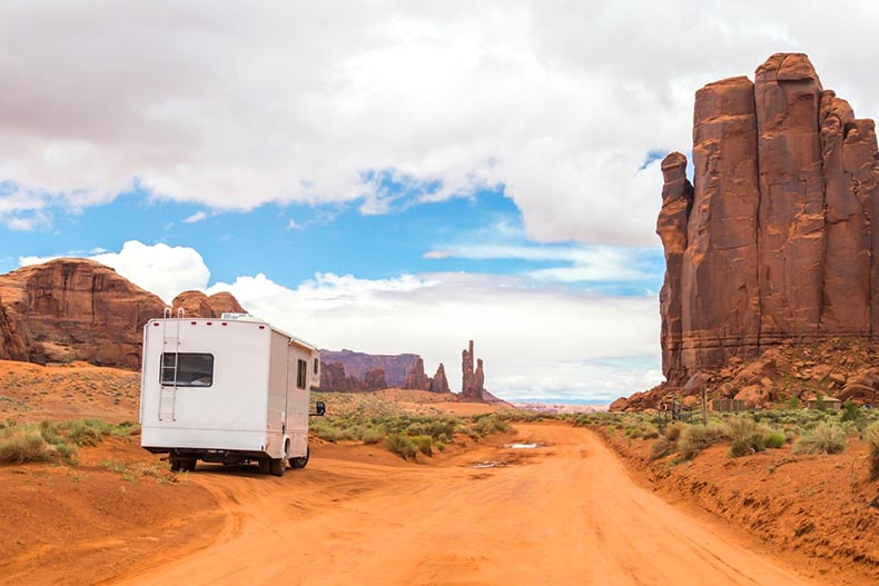 A white RV driving along a desert road lined with rock formations