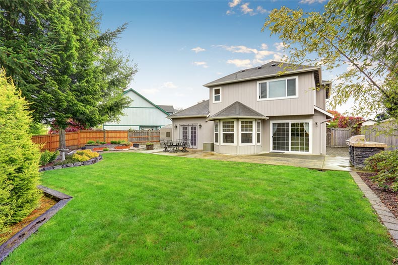 A spacious backyard behind a large beige house with a green lawn in a 55+ community