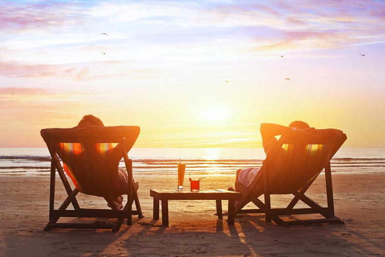 A retired couple in lounge chairs enjoying a sunset on the beach