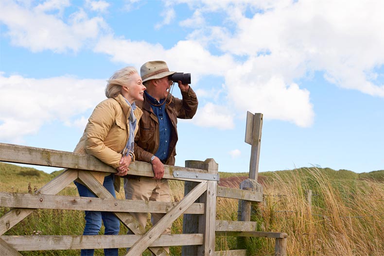 A senior couple standing by a fence and bird watching