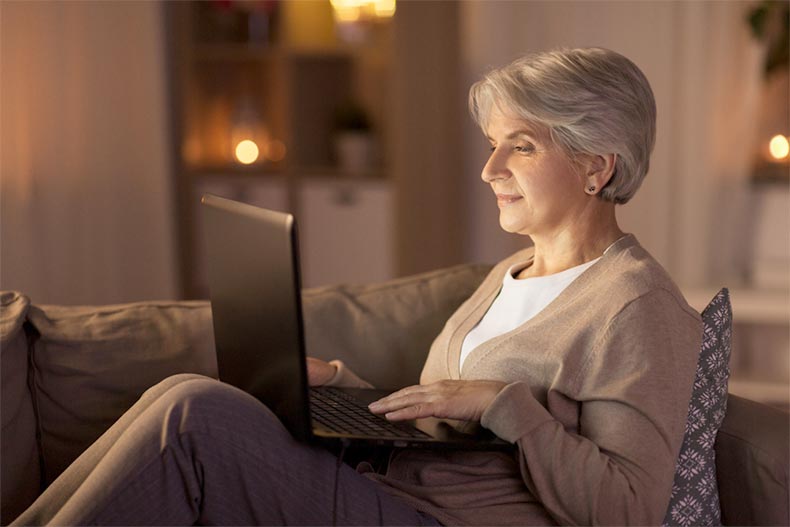 A senior woman at home in the evening and blogging on her laptop